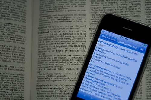 Cellphone with a dictionary app sitting on top of a physical dictionary.