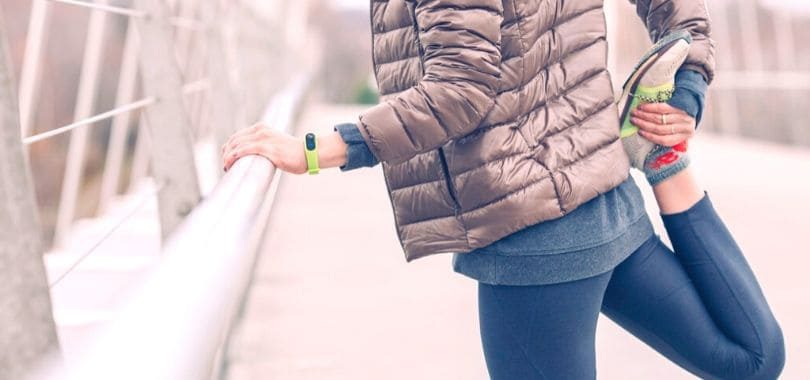 A college student stretching their leg while leaning against a railing.