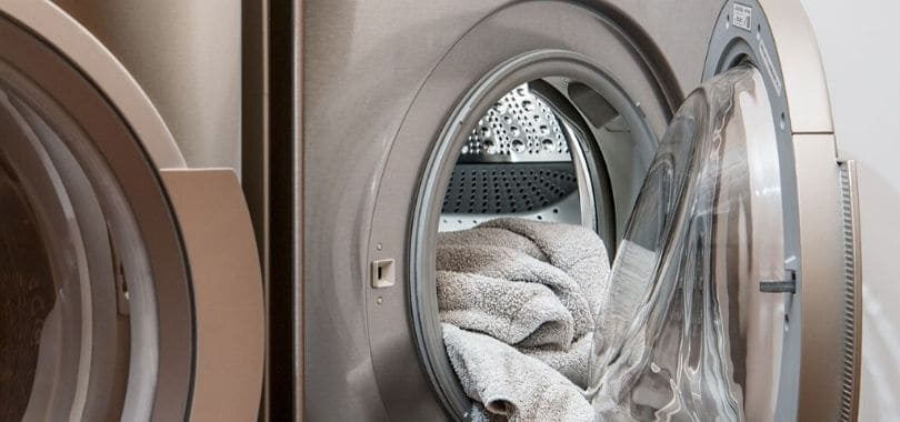 A silver washing machine with white towels inside the drum.