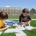 Two students studying outside on a blanket surrounded by books.