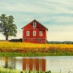 A red barn with a small pond in front of it.