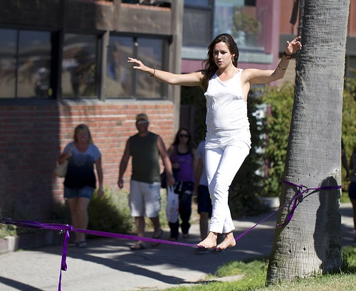 A girl walking on a purple tightrope that's tied to two trees.