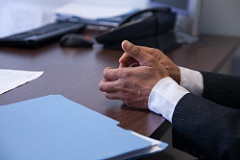 Well-dressed student in an interview with his hands folded on a desk.