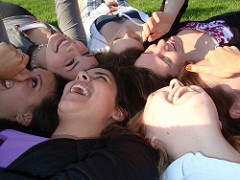 Several students laughing while lying on the grassy ground.