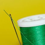 Sewing needle with a green spool of thread on a yellow background.