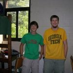 Two college students standing and smiling for picture taken inside their dorm room.