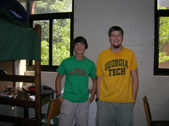 Two college students standing and smiling for picture taken inside their dorm room.
