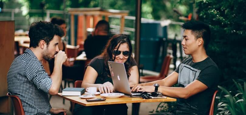 Three college students sitting at a table with a laptop and notebooks.