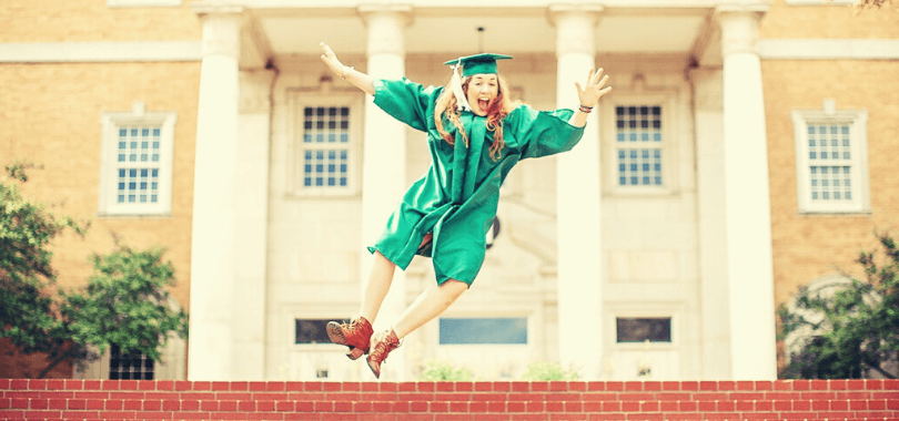 College student wearing a green graduation robe jumping.