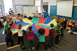Kids gather around the big color wheel fabric and holding it.