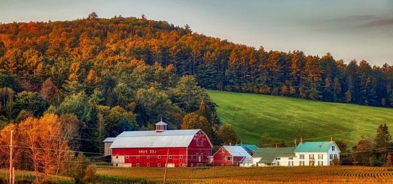 A red barn on grassy farmland with hills covered in trees behind it.