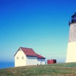 A lighthouse on a hill with a white and red house next to it.