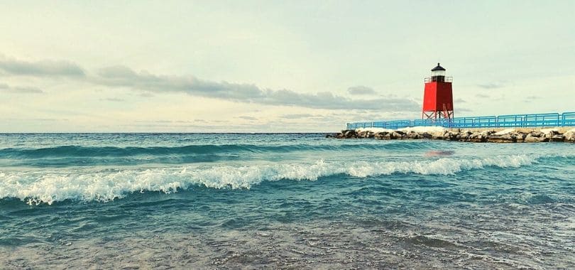 A red lighthouse by the shore of a beach.