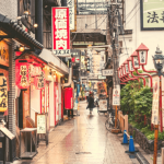 A person walking down a street filled with shops.