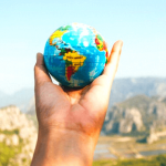 A student holding a small globe with mountains in the background.