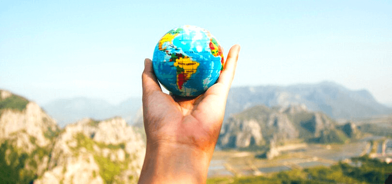 A student holding a small globe with mountains in the background.