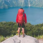 College student standing on top of a rock overlooking a lake.