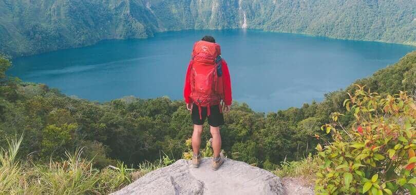 College student standing on top of a rock overlooking a lake.