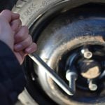 Hand holding a wrench attached to lug nut of the tire.