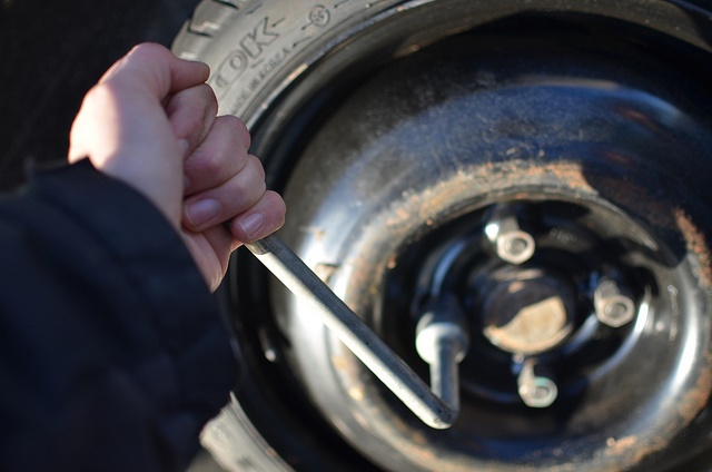 Hand holding a wrench attached to lug nut of the tire.