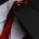 A graduation cap with a red tassel laying on top of a white shirt sleeve.