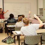 Students participating in a college class by raising their hands to answer the professor.