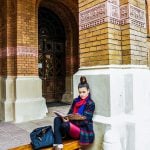 Female college student leaning on a building post while studying.