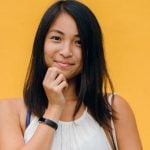 An Asian American student standing against an orange background.