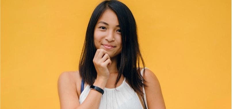 An Asian American student standing against an orange background.