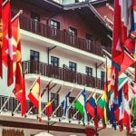 Multiple country flags on the balconies of white and brown buildings.