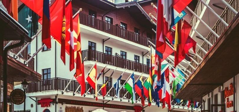 Multiple country flags on the balconies of white and brown buildings.