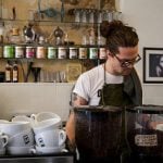 College student working as a barista mixing coffee on the counter.