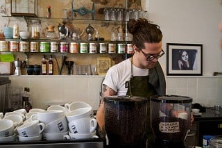 College student working as a barista mixing coffee on the counter.