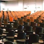 An empty lecture hall filled with brown desks.