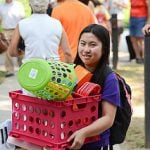 Student carrying her dorm supplies in a pink basket while moving into college.