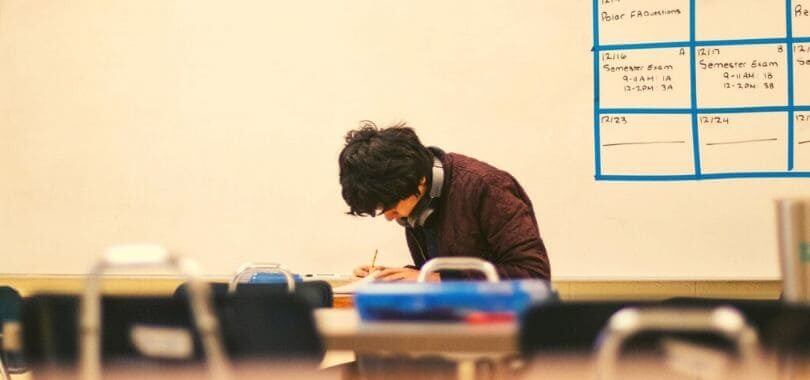 A high school student sitting in a classroom working on an assignment.