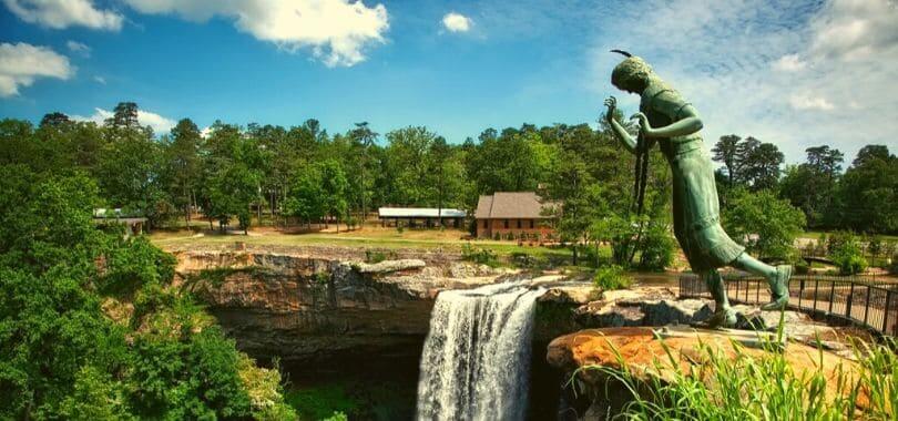 A statue of a person looking over a cliff by a waterfall.