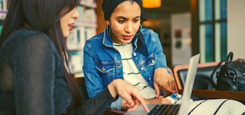 Two students sitting together and pointing at a laptop screen.