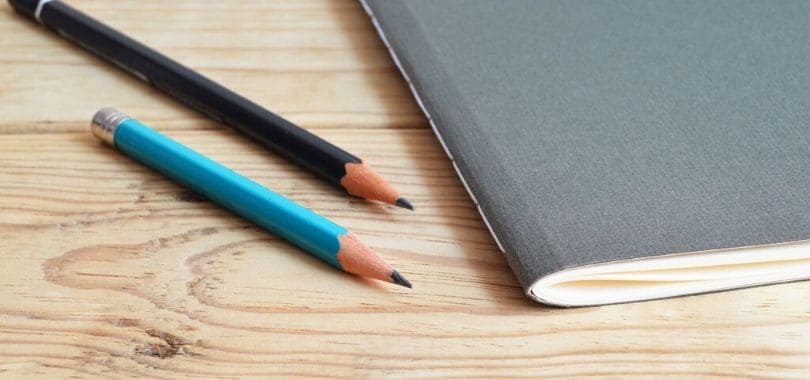 Two pencils laying next to a gray notebook.