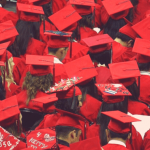 Graduating students in red robes and caps sitting together.