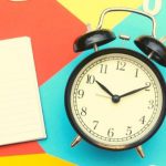 A black and white alarm clock next to an open notebook.