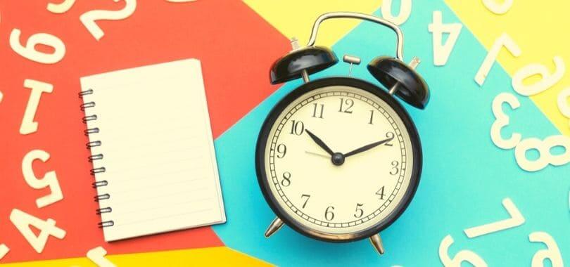 A black and white alarm clock next to an open notebook.