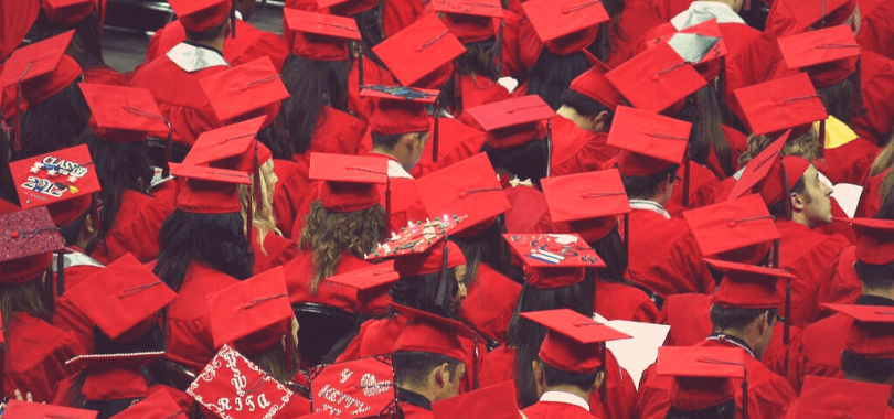 Graduating students in red robes and caps sitting together.