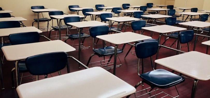 An empty high school classroom with white desks and blue chairs.