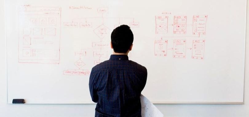 A student standing in front of a whiteboard with their back facing the camera.