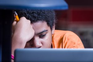 A student intently studying on his laptop while holding a pencil.
