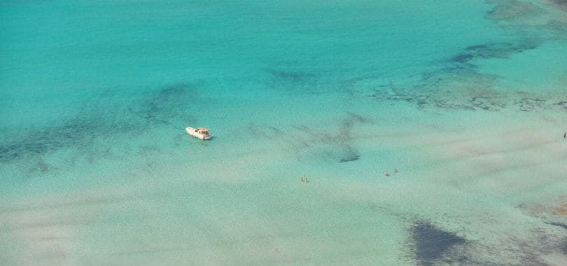 A overhead shot of the sea with a small white ship floating in it.