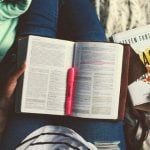 A student with a book and a pink highlighter in their lap