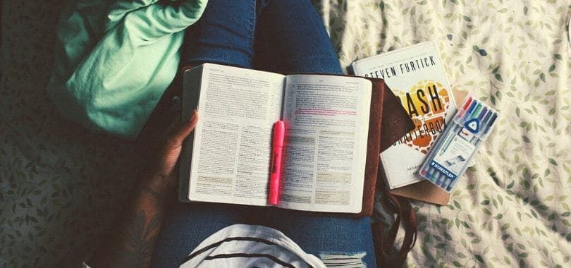 A student with a book and a pink highlighter in their lap