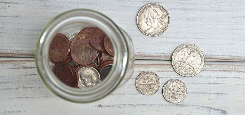A jar of coins with four coins scattered on the side.
